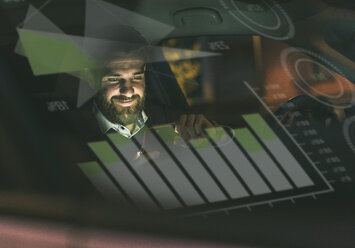 Smiling businessman with smartphone in car at night surrounded by data - UUF13404