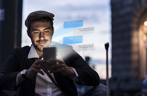 Junger Mann im Freien in der Abenddämmerung mit einem Text auf dem Smartphone - UUF13408