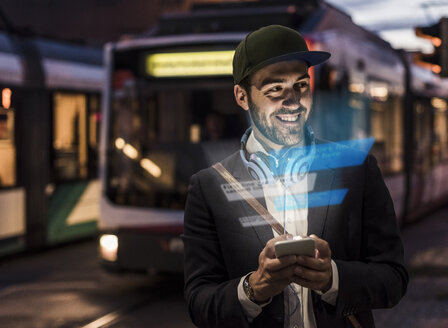 Junger Mann im Freien in der Abenddämmerung mit einem Text auf dem Smartphone - UUF13409