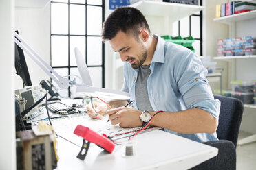 Lächelnder Techniker beim Löten einer Leiterplatte am Tisch im Elektroniklabor - CAVF39074