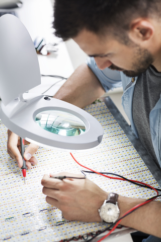 Ingenieur beim Löten von Leiterplatten mit Lupe in der Elektronikindustrie, lizenzfreies Stockfoto