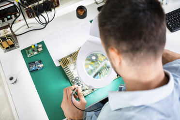 Technician soldering circuit board using magnifying glass at table - CAVF39081