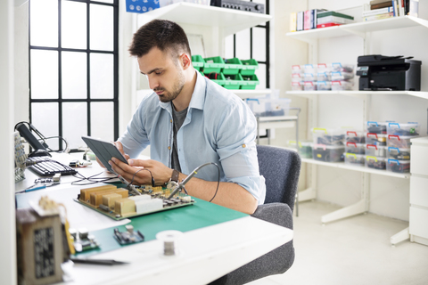 Seriöser Ingenieur, der einen Tablet-Computer bei der Arbeit am Tisch in der Elektronikindustrie benutzt, lizenzfreies Stockfoto