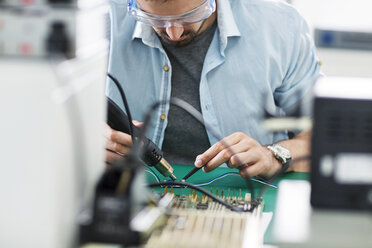 Serious technician working at table in electronics industry - CAVF39084