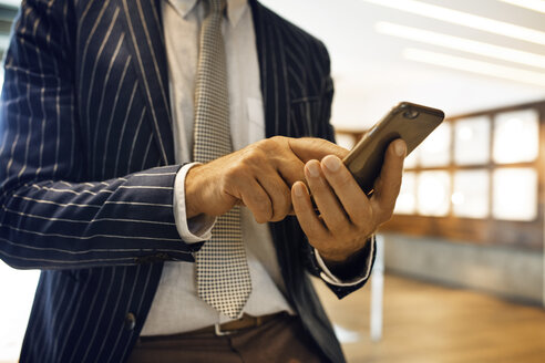 Mittelteil eines Geschäftsmannes, der ein Smartphone im Büro benutzt - CAVF39104