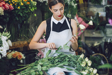 Female florist cutting stems of roses in flower shop - CAVF39168