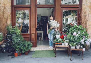 Female florist holding white flowers while standing entrance of shop - CAVF39177