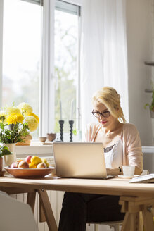 Frau benutzt einen Laptop, während sie am Tisch am Fenster sitzt - CAVF39184