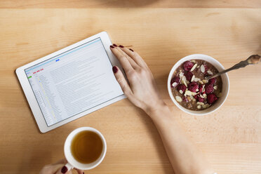 Cropped image of woman using tablet computer while having breakfast at table - CAVF39191