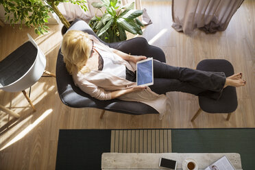 High angle view of woman using tablet computer while relaxing on armchair - CAVF39210