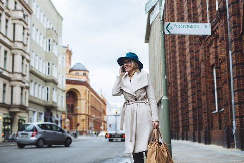 Glückliche Frau, die auf einer Straße in der Stadt steht und mit ihrem Handy telefoniert, lizenzfreies Stockfoto