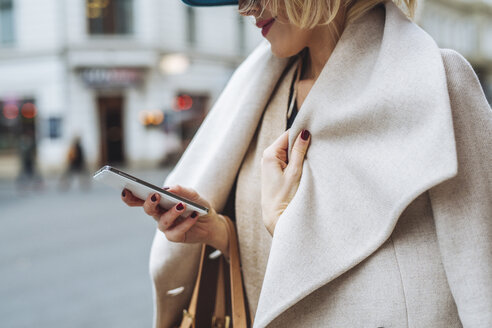 Mittelteil einer Frau, die ein Smartphone benutzt, während sie auf einer Straße steht - CAVF39230