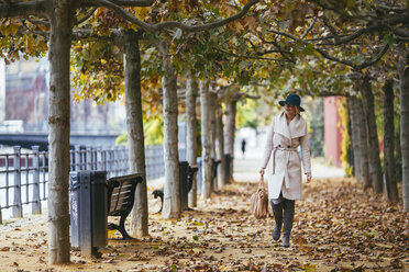 Frau mit Mantel, die im Herbst auf einem Fußweg im Park spazieren geht - CAVF39231
