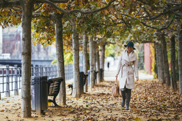 Woman wearing coat walking on footpath in park during autumn - CAVF39231