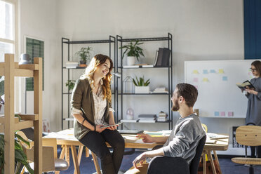 Smiling friends talking while sitting at desk in classroom - CAVF39285