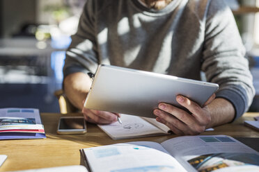 Mittelteil eines Mannes, der einen Tablet-Computer benutzt, während er am Tisch im Klassenzimmer lernt - CAVF39290