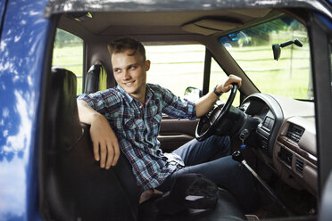 Happy man looking away while sitting in pick-up truck - CAVF39391