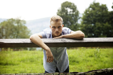 Portrait of man leaning on wooden fence in farm - CAVF39397