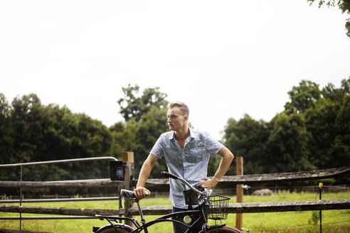 Mann mit Fahrrad auf einem Bauernhof bei klarem Himmel - CAVF39399