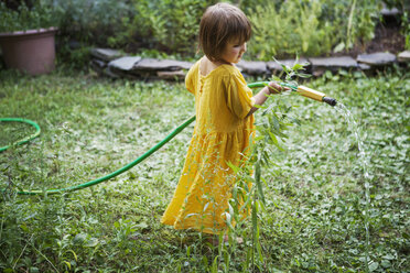 Girl watering plants with hose in backyard - CAVF39403