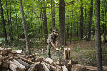 Man in hat cutting firewood with hammer in forest - CAVF39421