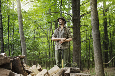 Glücklicher Mann, der wegschaut, während er bei Brennholz im Wald steht - CAVF39422