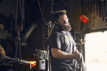 Schmied hält glühendes Metall mit einer Zange in der Werkstatt - CAVF39424