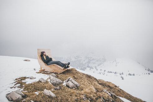 Österreich, Kitzbühel, Kitzbüheler Horn, junge Frau entspannt auf Liegestuhl im Winter mit Blick auf die Aussicht - GUSF00628