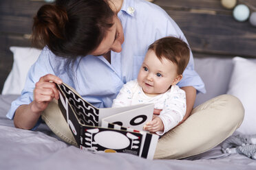 Mutter und Baby schauen sich zu Hause im Bett ein Bilderbuch an - ABIF00307