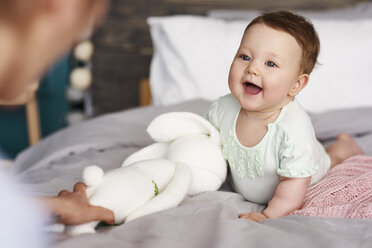 Glückliches Baby mit Kuscheltier auf dem Bett zu Hause, das seine Mutter anschaut - ABIF00318