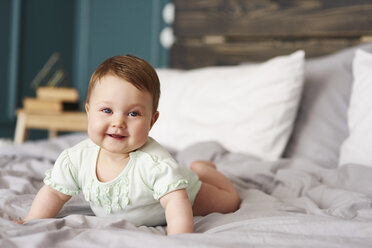 Porträt eines glücklichen Babys, das zu Hause auf dem Bett liegt - ABIF00320