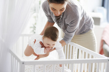 Mother laying her baby into crib at home - ABIF00326