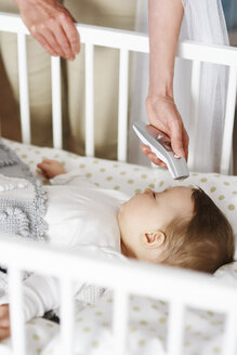 Mutter mit digitalem Thermometer prüft die Temperatur des Babys im Kinderbett - ABIF00332