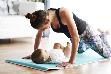 Mother with baby exercising on yoga mat at home - ABIF00333