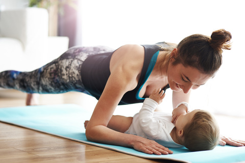 Mutter mit Baby übt auf Yogamatte zu Hause, lizenzfreies Stockfoto