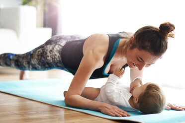 Mother with baby exercising on yoga mat at home - ABIF00337