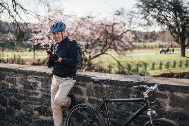 Älterer Mann mit Fahrradhelm und Smartphone - GUSF00636