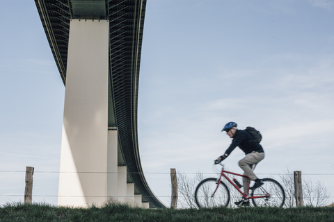 Älterer Mann auf dem Fahrrad, unter einer Brücke, lizenzfreies Stockfoto