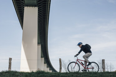 Senior man riding bike, under bridge - GUSF00638