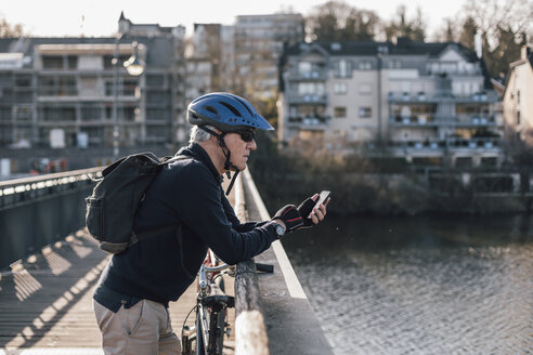Älterer Mann mit Fahrradhelm benutzt Smartphone auf Brücke - GUSF00639