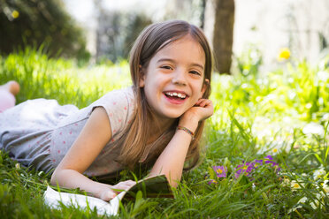 Smiling girl lying on meadow, reading a book - LVF06869