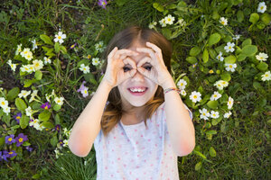 Girl looking through fingers, lying on flower meadow, top view - LVF06871