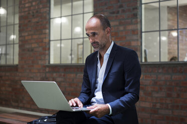 Businessman using laptop computer while sitting on seat against office - CAVF39447