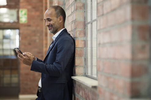 Seitenansicht eines Geschäftsmannes, der ein Smartphone benutzt, während er an einer Mauer steht - CAVF39449