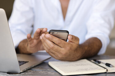 Midsection of businessman using smart phone while sitting at table in office - CAVF39455