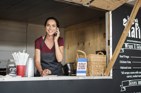 Porträt eines lächelnden weiblichen Verkäufers, der mit seinem Smartphone spricht, während er in einem Imbisswagen arbeitet, lizenzfreies Stockfoto