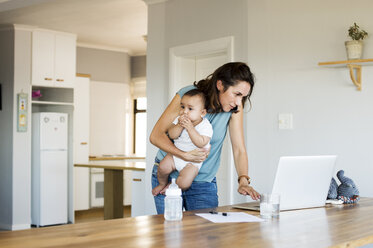 Woman using laptop computer while sitting with son at home - CAVF39498