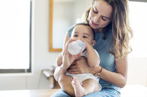 Mother feeding baby boy while sitting on table at home - CAVF39500