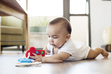 Baby boy playing with toys while lying on floor at home - CAVF39512