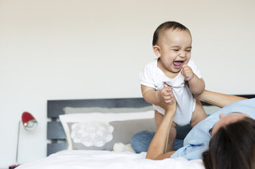 Cheerful baby boy playing with mother on bed at home - CAVF39519